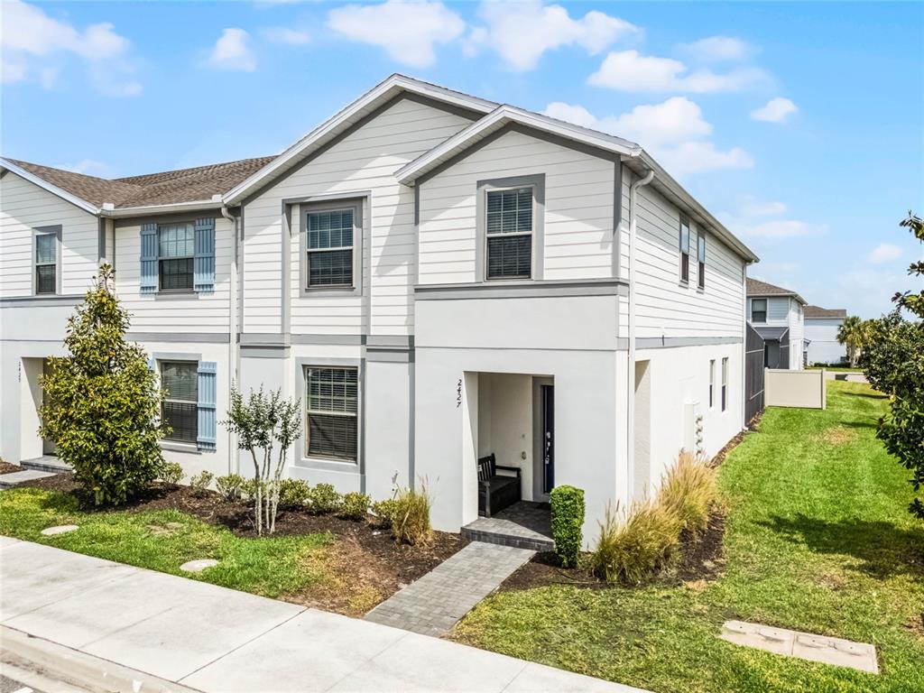 A two-story townhouse with white siding and stucco features a front entryway and landscaped yard — 2427 DUBAI STREET, KISSIMMEE, FL