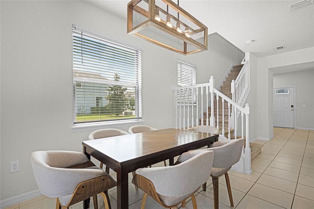 A dining area features a wooden table, upholstered chairs, a rectangular chandelier, and carpeted stairs — 2427 DUBAI STREET, KISSIMMEE, FL