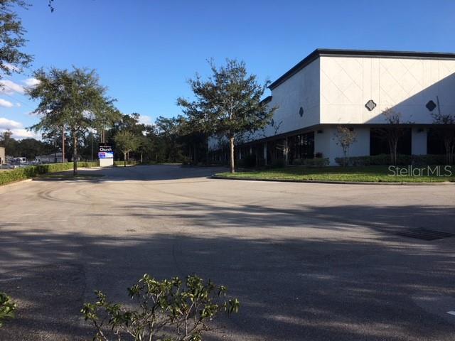 A paved parking lot sits in front of a white commercial building with trees — 6859 EDGEWATER COMMERCE PARKWAY, ORLANDO, FL