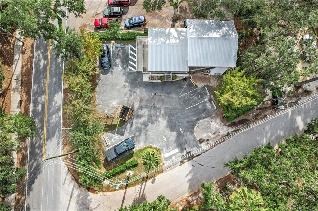 An aerial view shows a building with a metal roof, parking lot, and surrounding trees — 10460 W NEW YORK STREET, HOMOSASSA, FL
