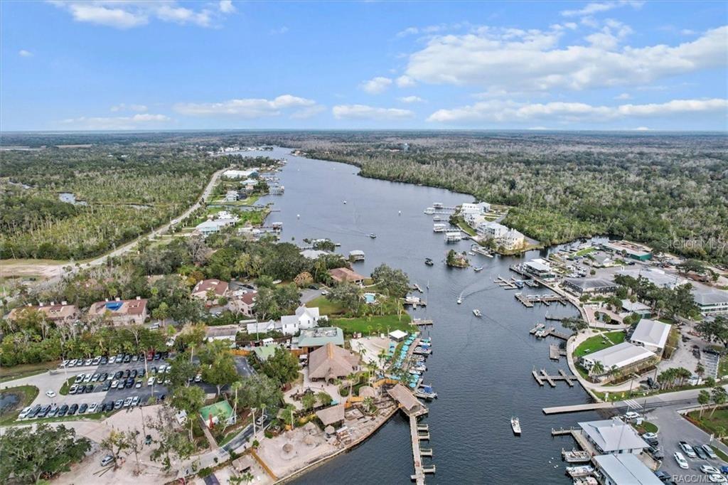 An aerial view shows a riverfront area with a marina, boat docks, and surrounding buildings — 10460 W NEW YORK STREET, HOMOSASSA, FL