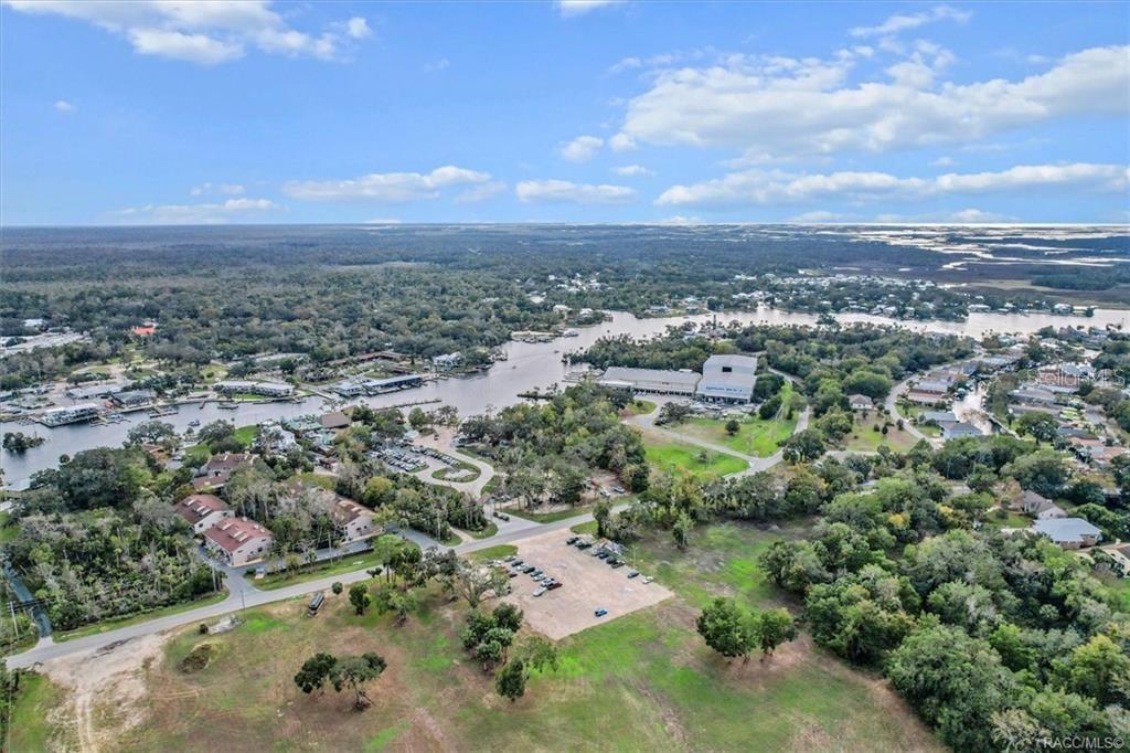 An aerial view shows a waterfront area with a parking lot, trees, and buildings — 10460 W NEW YORK STREET, HOMOSASSA, FL