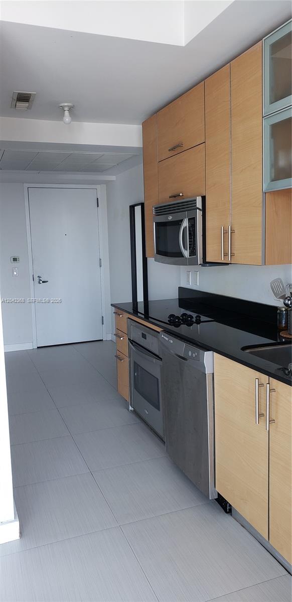 A kitchen features light wood cabinets, black countertops, stainless steel appliances, and light tile flooring — 60 SW 13th St # 1621, Miami FL 33130, MIAMI, FL