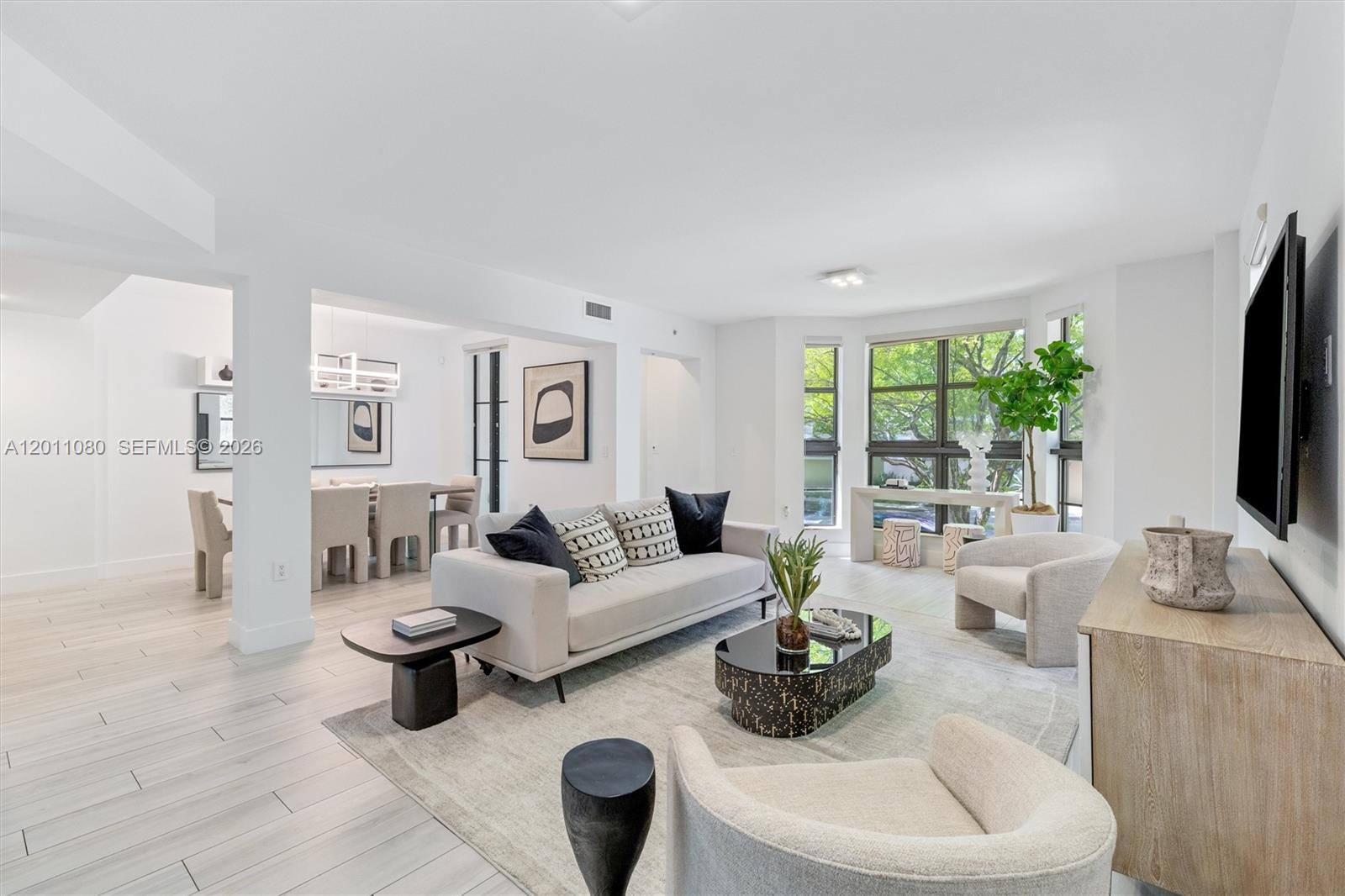 A bright living room features light wood-look flooring, a neutral sofa, and large windows — 1650 Galiano St, Coral Gables FL 33134, CORAL GABLES, FL