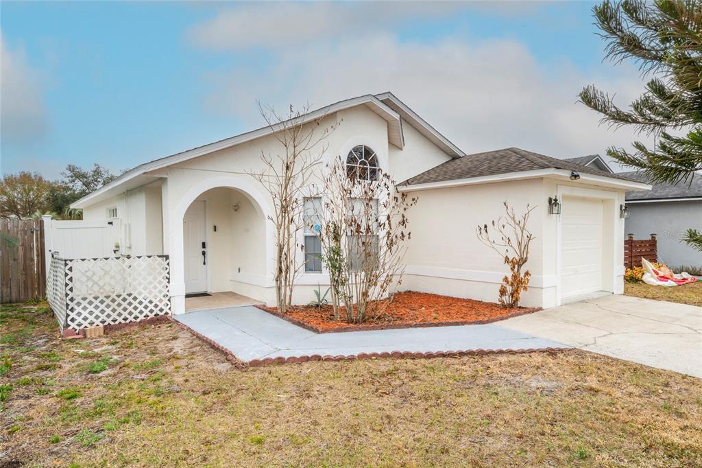 A single-story house with white stucco siding, a front-facing garage, and a small garden bed — 10201 VISTA COVE LANE, ORLANDO, FL