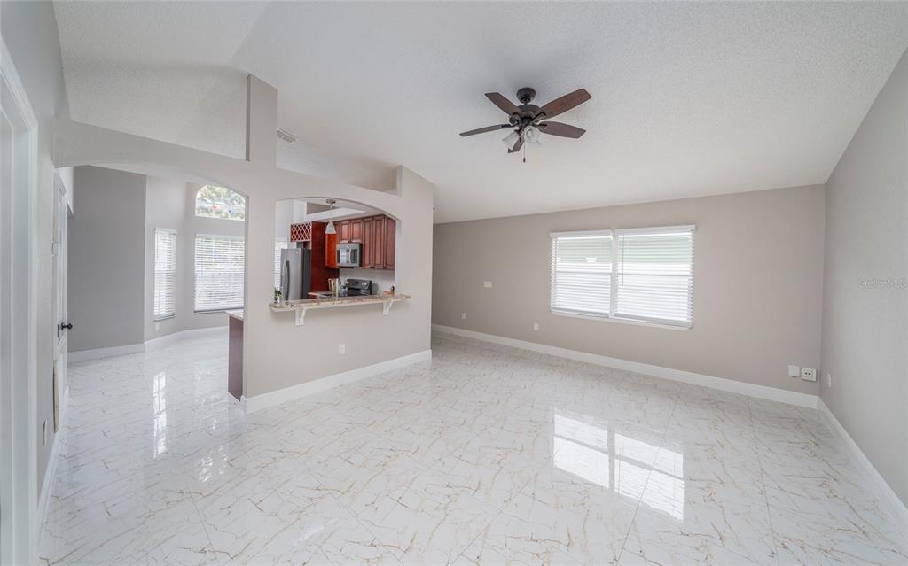 A living room with white marble-look tile floors, a ceiling fan, and an open kitchen — 10201 VISTA COVE LANE, ORLANDO, FL