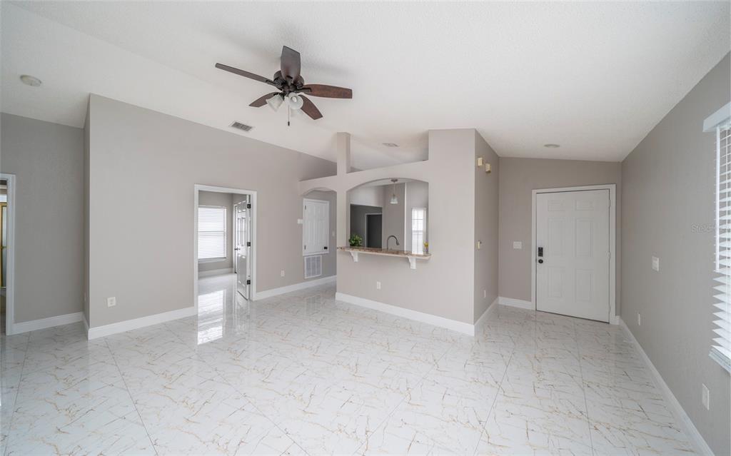 A living room with white marble-patterned tile floors, a ceiling fan, and a kitchen pass-through — 10201 VISTA COVE LANE, ORLANDO, FL