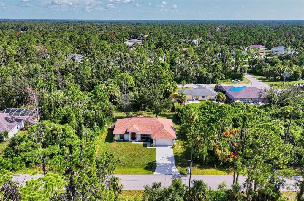 An aerial view shows a single-story house with a red roof surrounded by dense trees — 2634 TWINKLE AVENUE, NORTH PORT, FL