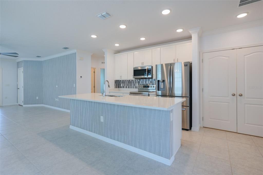 A kitchen features white cabinets, stainless steel appliances, a quartz island, and light-colored tile flooring — 173 VILLAVISTA COURT, DAVENPORT, FL