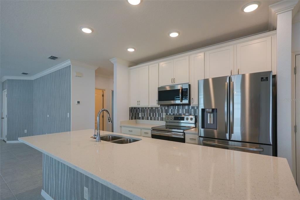 A modern kitchen features white cabinets, stainless steel appliances, and a large quartz-topped island — 173 VILLAVISTA COURT, DAVENPORT, FL