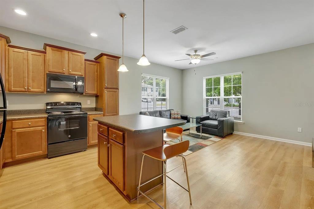 A kitchen with wooden cabinets and a center island opens into a living area — 3660 TYSON GREEN WAY UNIT 707, TALLAHASSEE, FL