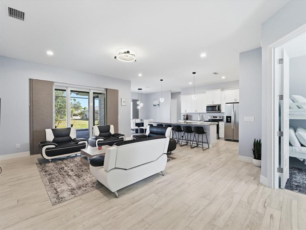 An open-concept living room and kitchen featuring light wood floors and modern black-and-white furniture — 17 PINE VALLEY LANE, ROTONDA WEST, FL