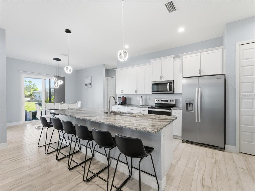 A modern kitchen features white cabinets, granite countertops, a large island, and black bar stools — 17 PINE VALLEY LANE, ROTONDA WEST, FL