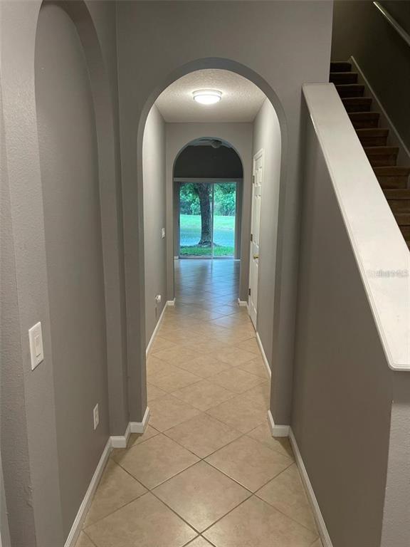 A hallway with arched openings, tile flooring, and a staircase leads to a sliding glass door — 16265 OLD ASH LOOP, ORLANDO, FL