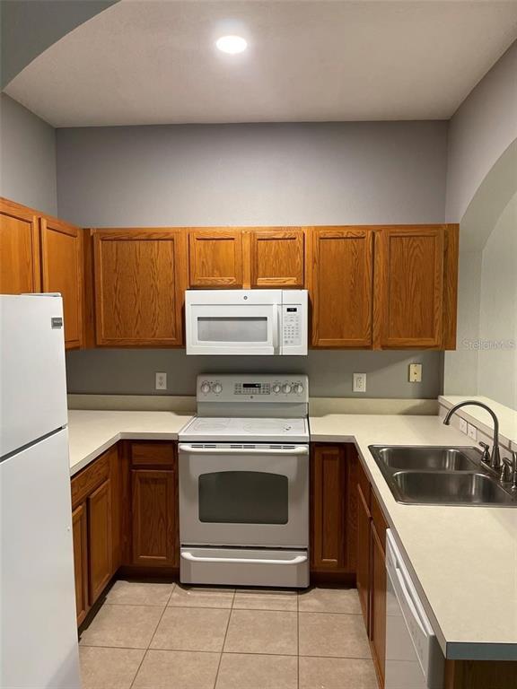 A kitchen features oak cabinets, white appliances, light countertops, and tile flooring — 16265 OLD ASH LOOP, ORLANDO, FL