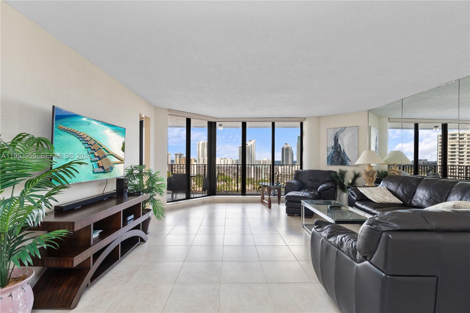 A living room features tile flooring, black leather furniture, a media console, and floor-to-ceiling windows — 300 Three Islands Blvd # 417, Hallandale Beach FL 33009, HALLANDALE BEACH, FL