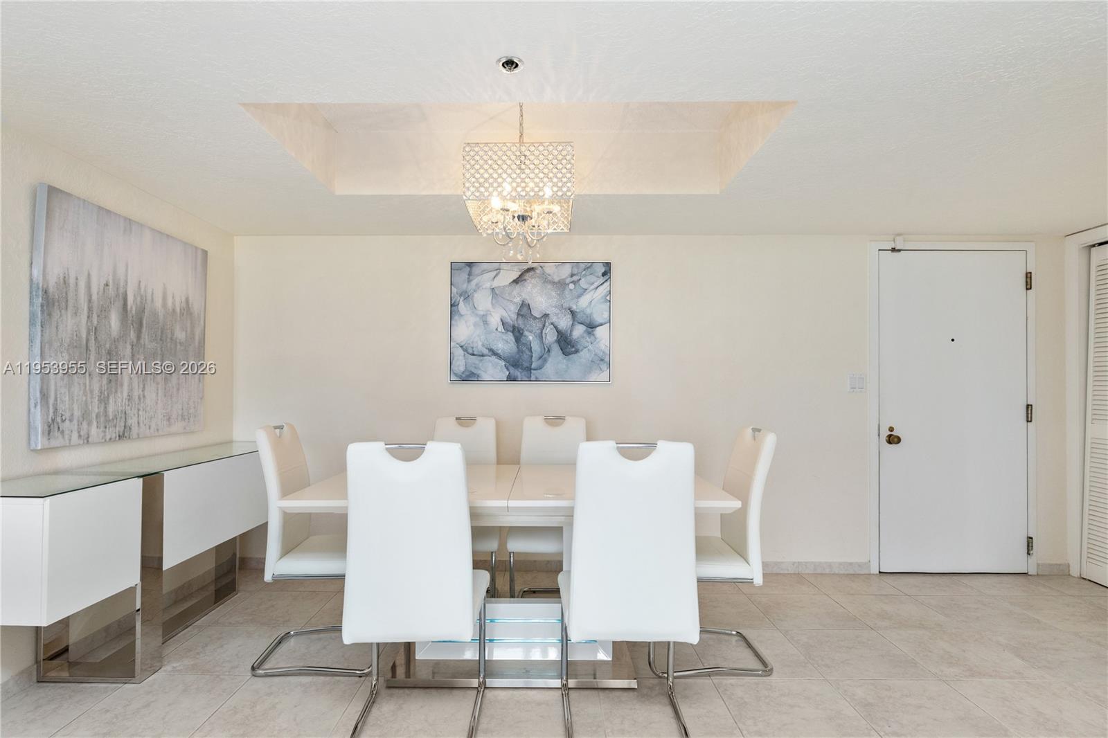 A dining room features a white table, six chairs, a crystal chandelier, and wall art — 300 Three Islands Blvd # 417, Hallandale Beach FL 33009, HALLANDALE BEACH, FL