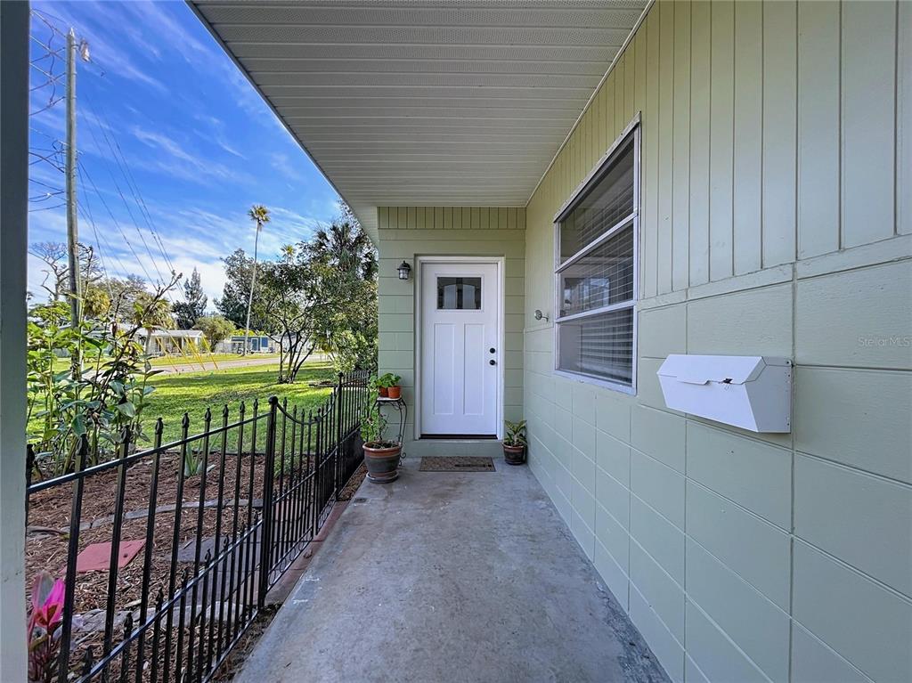 A covered concrete porch leads to a white front door on a light green house — 4042 ARKANSAS AVENUE NE, ST PETERSBURG, FL