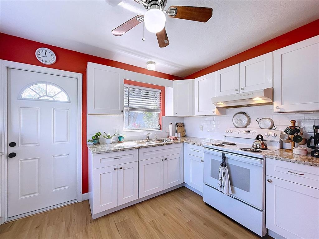 A kitchen with white cabinets, granite countertops, red walls, and light wood-look flooring — 4042 ARKANSAS AVENUE NE, ST PETERSBURG, FL
