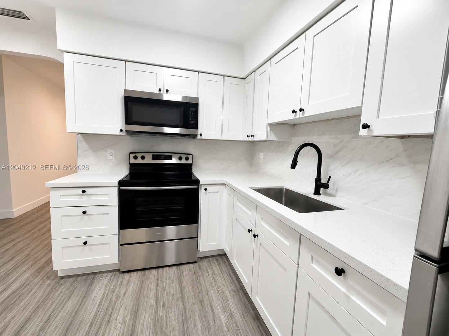 A kitchen features white cabinets, quartz countertops, stainless steel appliances, and a black faucet — 730 SW 5th St # 1, Hallandale Beach FL 33009, HALLANDALE BEACH, FL