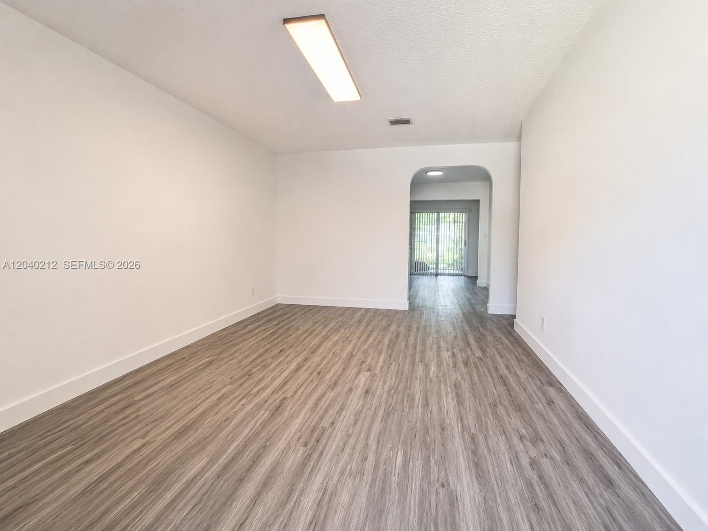 An empty room with white walls, wood-look flooring, and an arched doorway leading outside — 730 SW 5th St # 1, Hallandale Beach FL 33009, HALLANDALE BEACH, FL