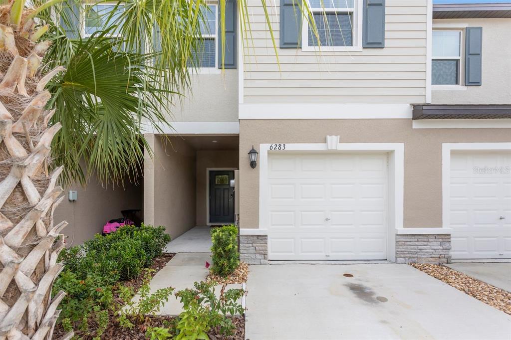 The exterior of a two-story townhouse features a garage, a covered entryway, and a palm tree — 6283 SHINER STREET, LAND O LAKES, FL
