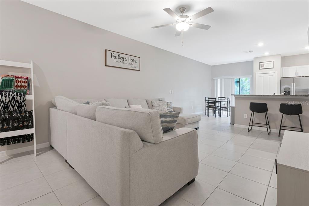 A living room with light tile floors, a gray sectional sofa, and an open kitchen area — 6283 SHINER STREET, LAND O LAKES, FL