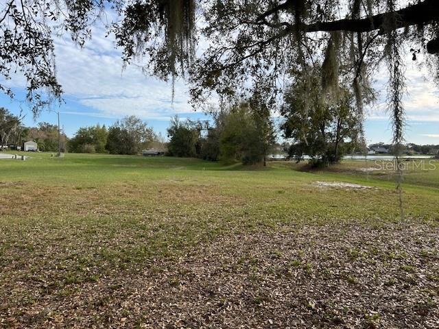 A grassy, open lot features scattered trees with Spanish moss and a distant view of water — CANVASBACK PLACE, LAKELAND, FL