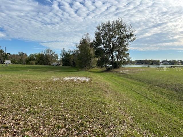 A grassy, vacant lot features scattered trees and a view of a distant lake — CANVASBACK PLACE, LAKELAND, FL