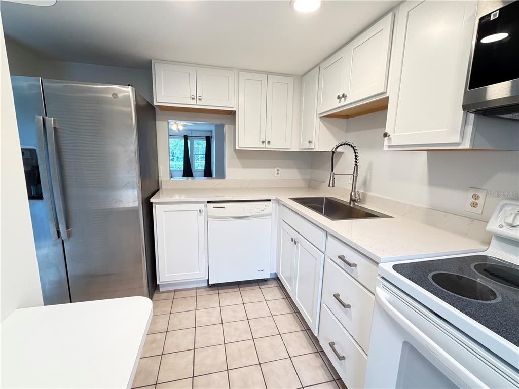 A kitchen features white cabinets, stainless steel appliances, a tile floor, and quartz countertops — 333 LAKE HOWARD DRIVE NW UNIT 211B, WINTER HAVEN, FL