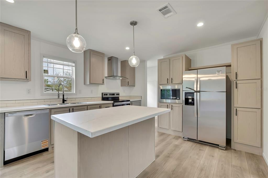 A modern kitchen features light wood cabinets, stainless steel appliances, and a central island — 5342 S ISABEL TERRACE, HOMOSASSA, FL