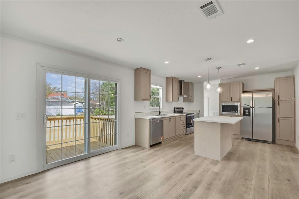 A modern kitchen features light wood cabinets, stainless steel appliances, an island, and sliding doors — 5342 S ISABEL TERRACE, HOMOSASSA, FL