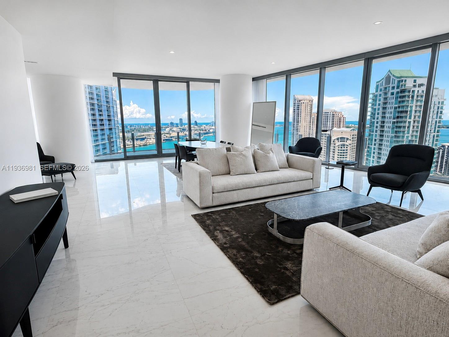 A modern living room features white marble floors, floor-to-ceiling windows, and panoramic city and water views — 300 Biscayne Blvd Way # 3201, Miami FL 33130, MIAMI, FL