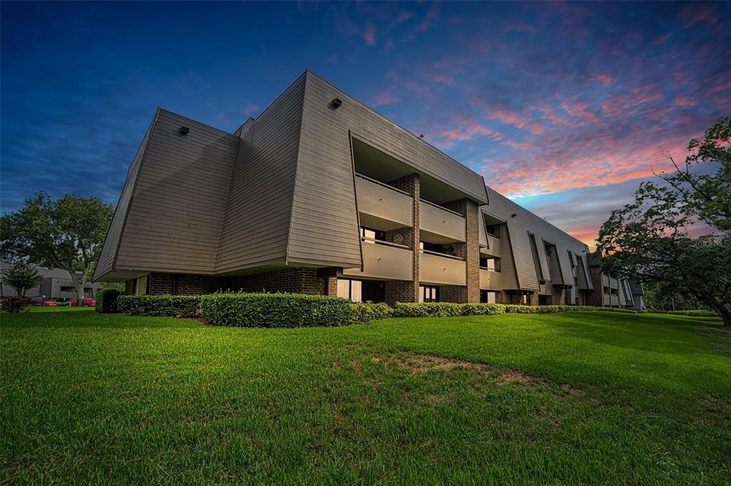 A low-angle view of a multi-story apartment building with angled siding and balconies at sunset — 36750 US HIGHWAY 19 N UNIT 20-209, PALM HARBOR, FL