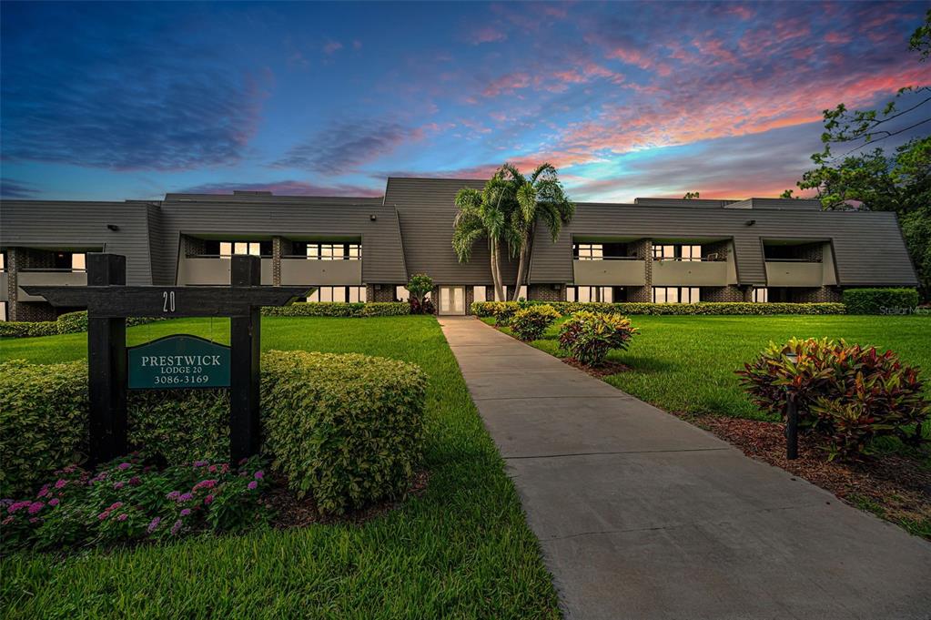 A two-story apartment building with a walkway leading to the entrance under a sunset sky — 36750 US HIGHWAY 19 N UNIT 20-209, PALM HARBOR, FL