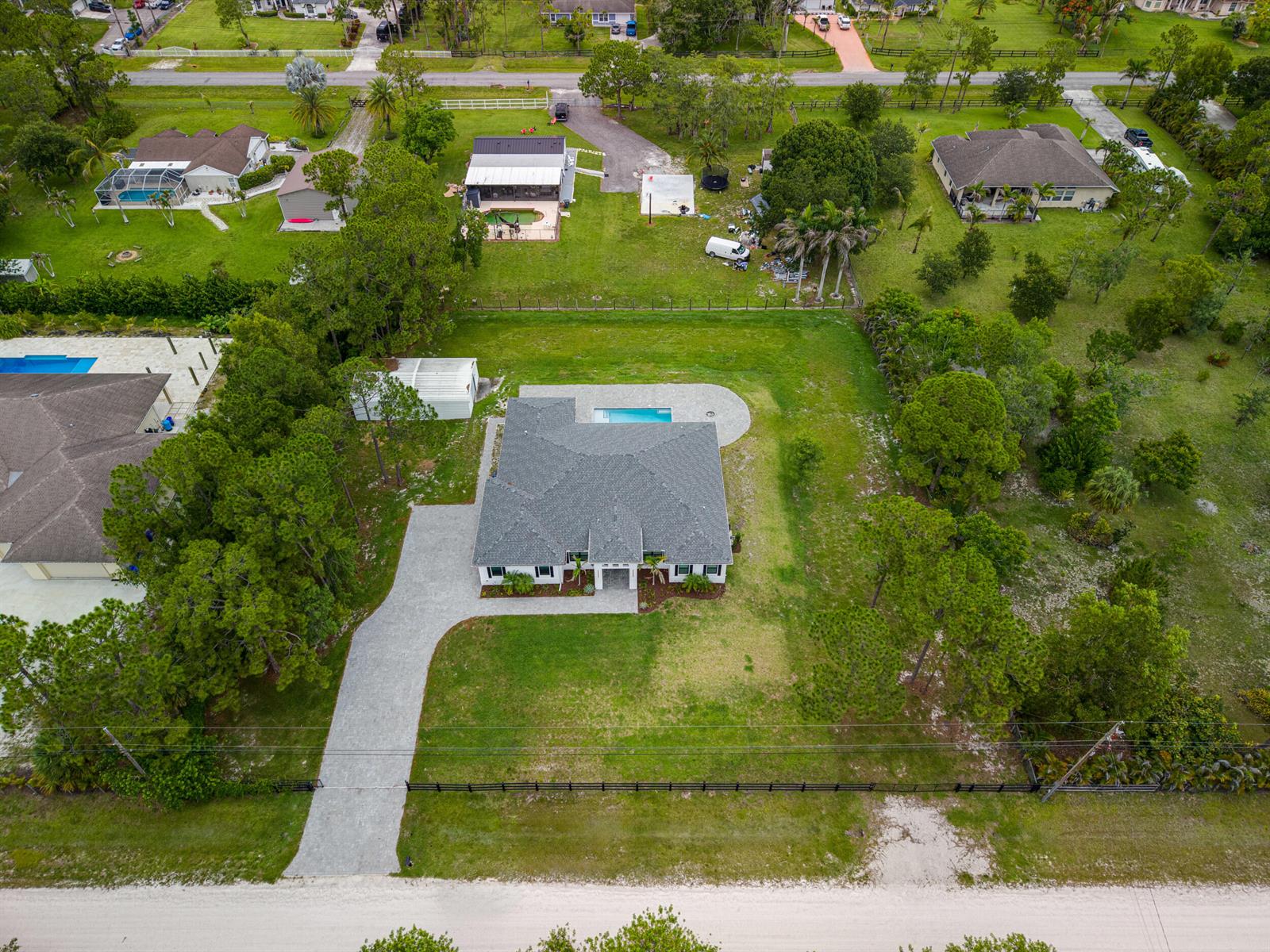 An aerial view shows a single-story house with a grey roof, pool, and paved driveway — 17655 44th Place N, FL 33470, FL