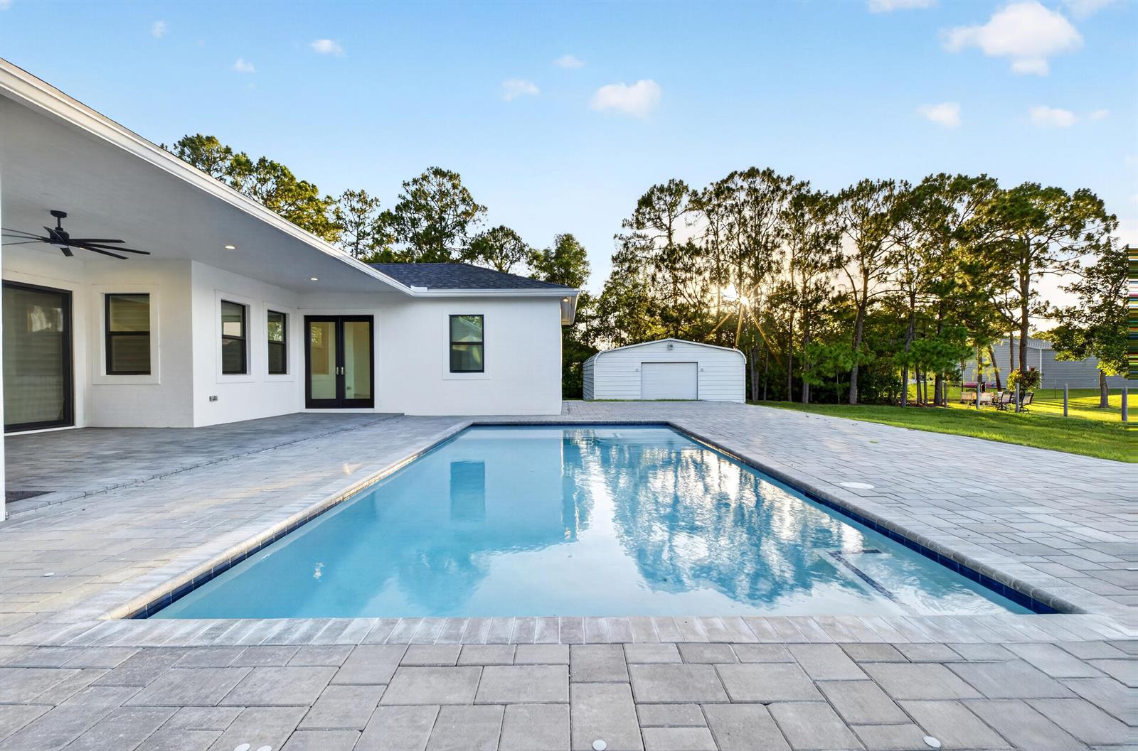 A rectangular swimming pool sits on a paved patio beside a white house and shed — 17655 44th Place N, FL 33470, FL