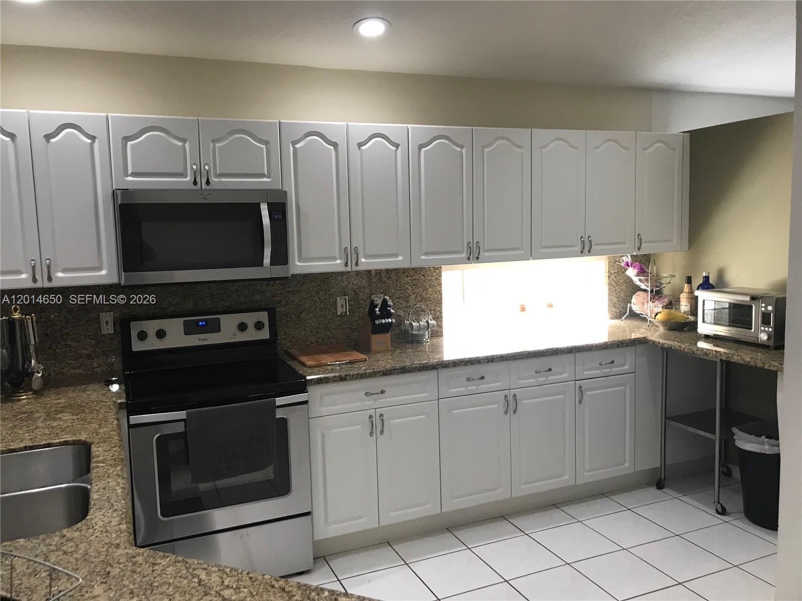 A kitchen features white cabinetry, granite countertops, stainless steel appliances, and white floor tiles — 16654 SW 103rd Ln, Miami FL 33196, MIAMI, FL