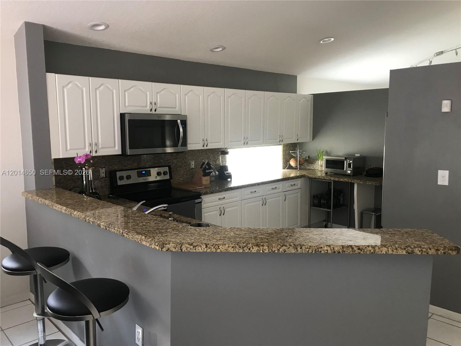 A kitchen features white cabinets, granite countertops, a breakfast bar, and gray walls — 16654 SW 103rd Ln, Miami FL 33196, MIAMI, FL