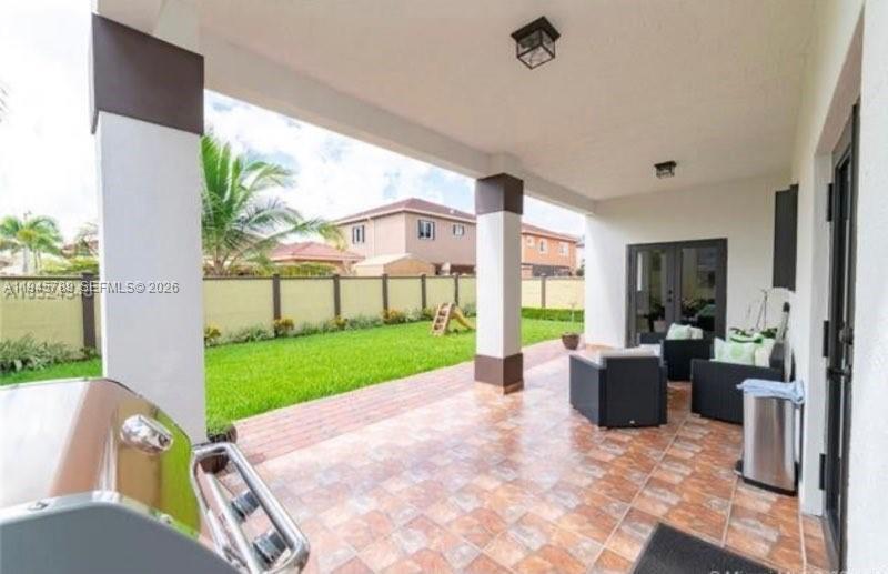 A covered patio with tiled flooring overlooks a grassy backyard enclosed by a perimeter wall — 16588 SW 44 Street, Kendall FL 33185, KENDALL, FL