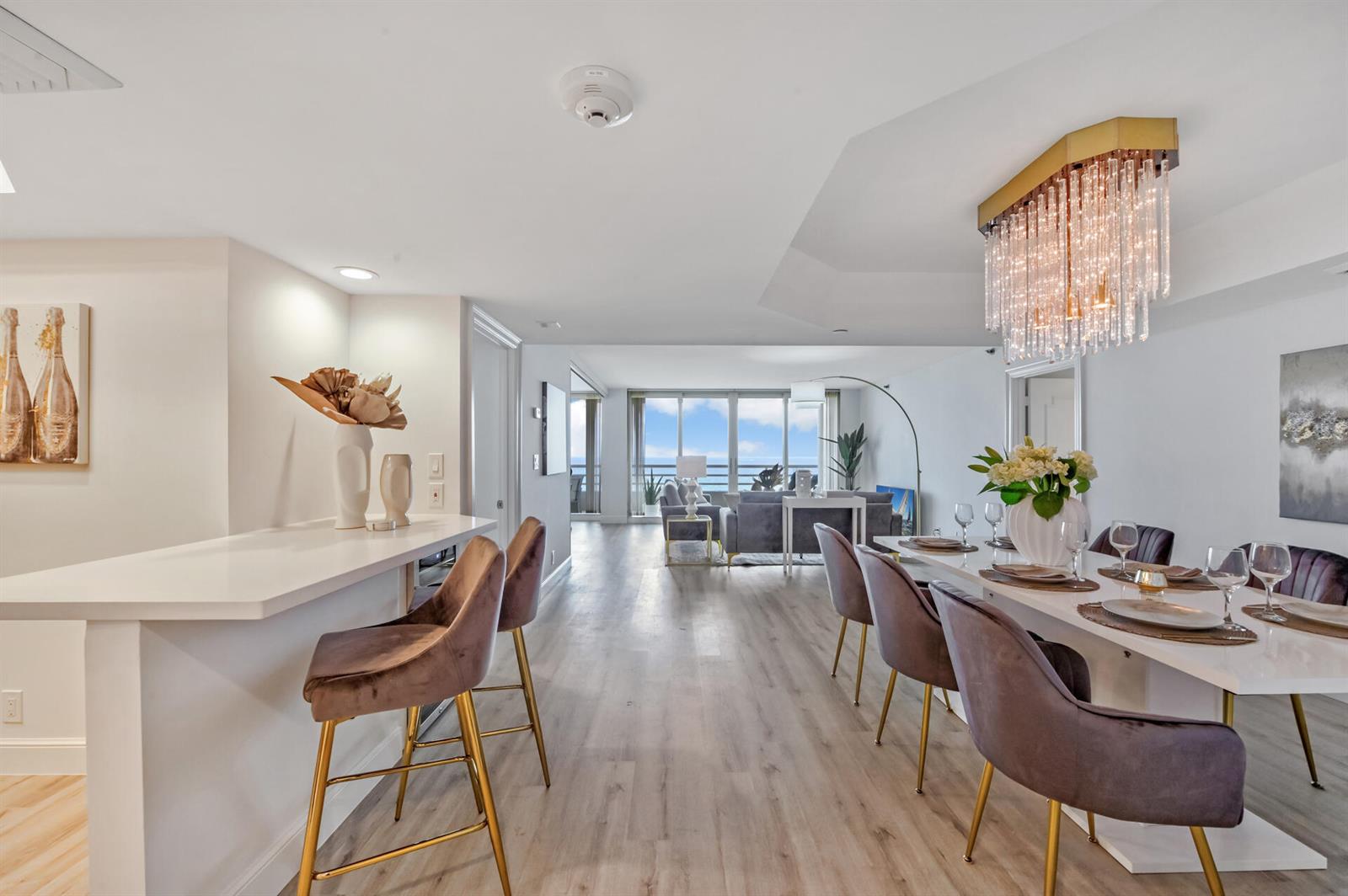 An open-concept dining and living area features a crystal chandelier, bar seating, and ocean views — 4101 N Ocean Boulevard Unit 1008, Boca Raton FL 33431, BOCA RATON, FL