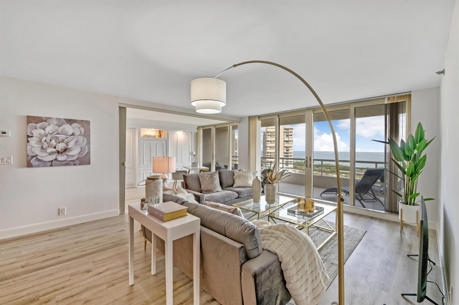 A living room features a grey sofa, glass coffee tables, and a balcony overlooking the ocean — 4101 N Ocean Boulevard Unit 1008, Boca Raton FL 33431, BOCA RATON, FL