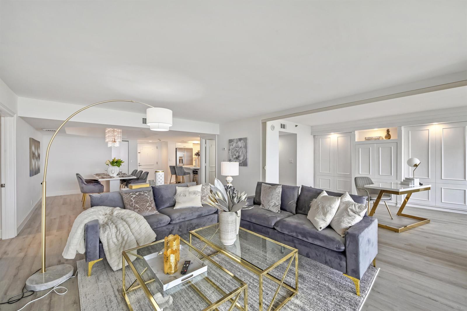 A living room features two gray velvet sofas, glass coffee tables, and a gold floor lamp — 4101 N Ocean Boulevard Unit 1008, Boca Raton FL 33431, BOCA RATON, FL