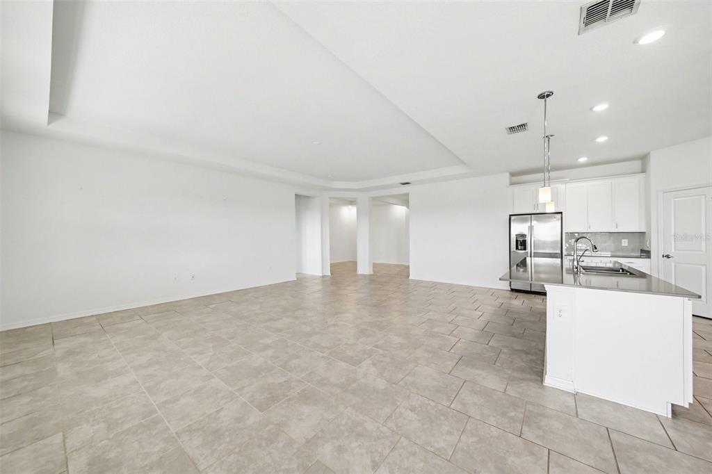 An open-concept living area features light tile flooring, white walls, and an adjacent kitchen — 6079 CLAYSTONE WAY, MOUNT DORA, FL