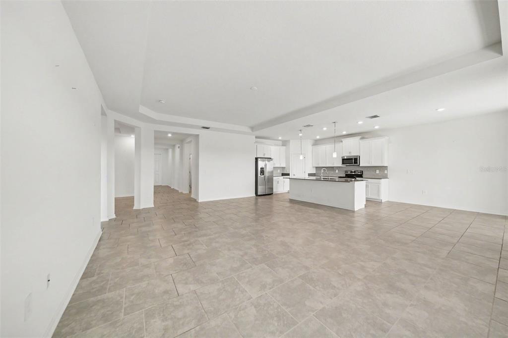 A spacious, open-concept kitchen and living area featuring white cabinetry, tile flooring, and recessed lighting — 6079 CLAYSTONE WAY, MOUNT DORA, FL