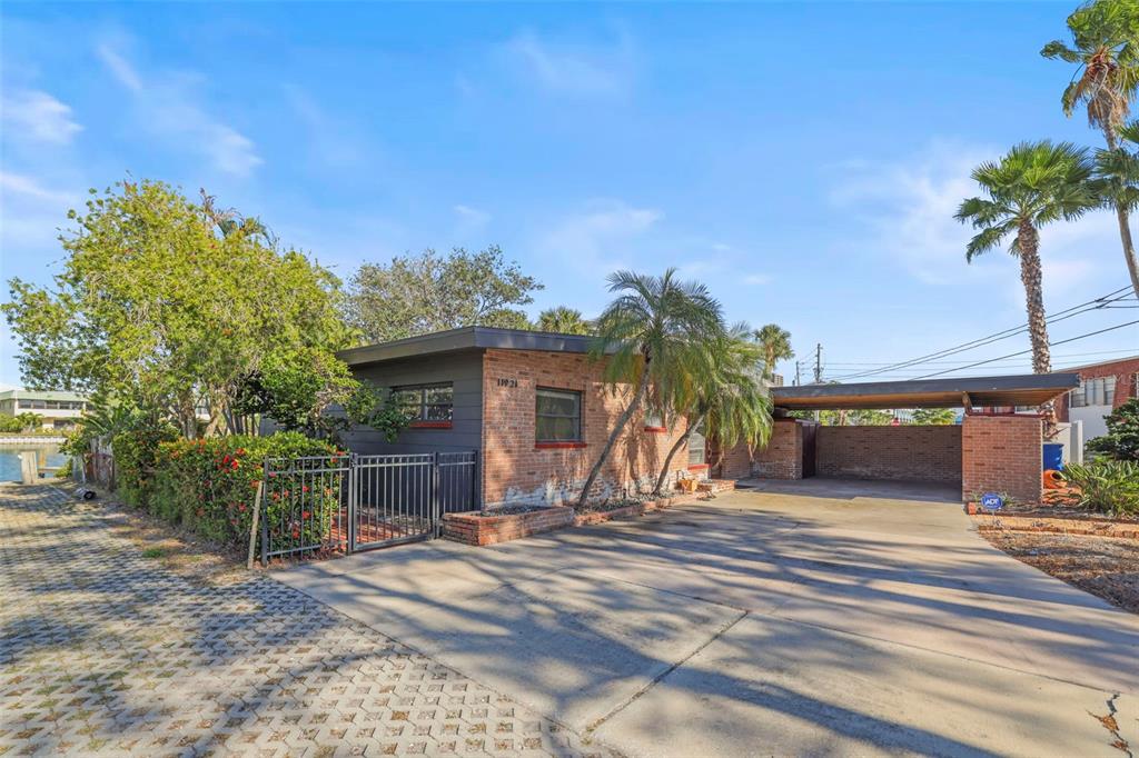 A single-story brick house features a flat roof, a carport, and a fenced side yard — 11921 LAGOON LANE, TREASURE ISLAND, FL