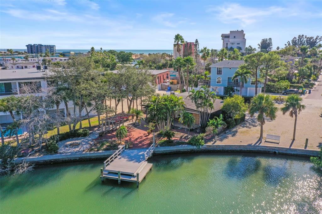 An aerial view shows a waterfront house with a wooden dock and a paved patio — 11921 LAGOON LANE, TREASURE ISLAND, FL