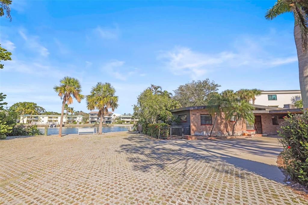 A brick house sits beside a waterfront area with a paved lot and palm trees — 11921 LAGOON LANE, TREASURE ISLAND, FL