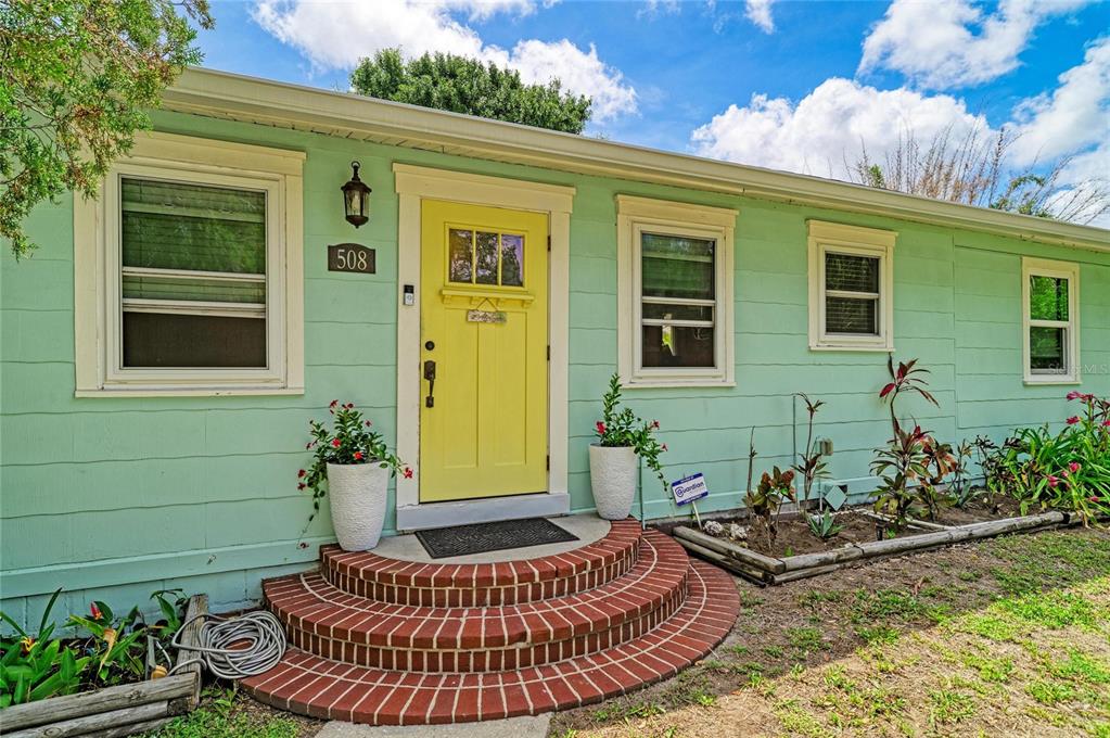 A light green house exterior features a yellow front door and curved brick steps — 508 16TH AVENUE W, PALMETTO, FL