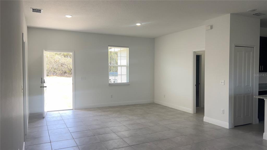 An empty room with light-colored tile flooring, white walls, a window, and an open door — 16390 SW 17TH TERRACE ROAD, OCALA, FL